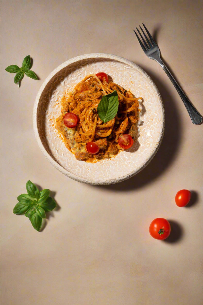 Plate of pasta with cherry tomatoes and basil leaves on a textured surface with a fork.