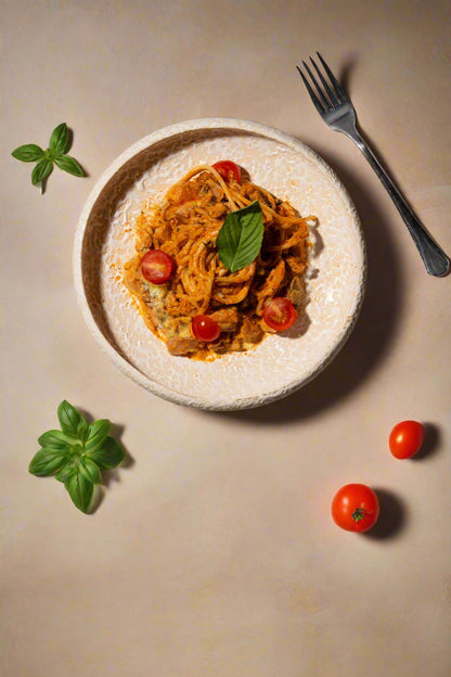Plate of pasta with cherry tomatoes and basil leaves on a textured surface with a fork.